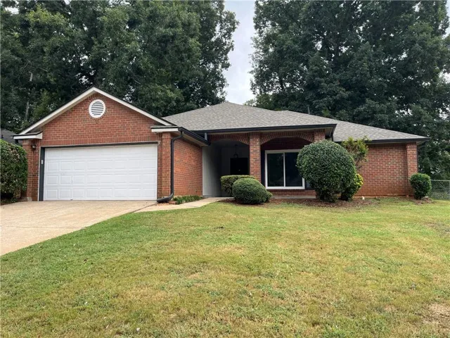 Brick exterior with a gabled roofline, attached garage, concrete driveway, and established landscaping
