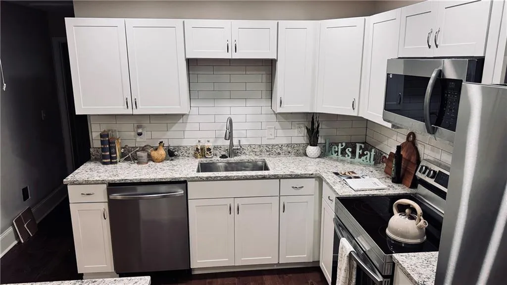 Kitchen featuring stainless steel appliances, white cabinets, decorative backsplash, light stone counters, and dark wood-style floors