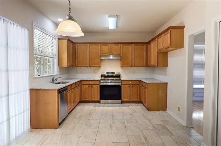 U-shaped kitchen with wood cabinetry, light-toned countertops, tile backsplash, stainless steel appliances, and tile flooring