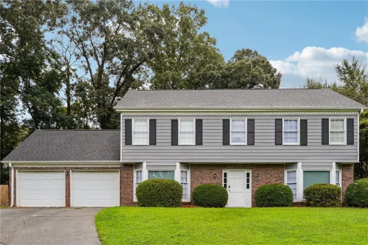Colonial home with brick siding, roof with shingles, a garage, asphalt driveway, and a front yard