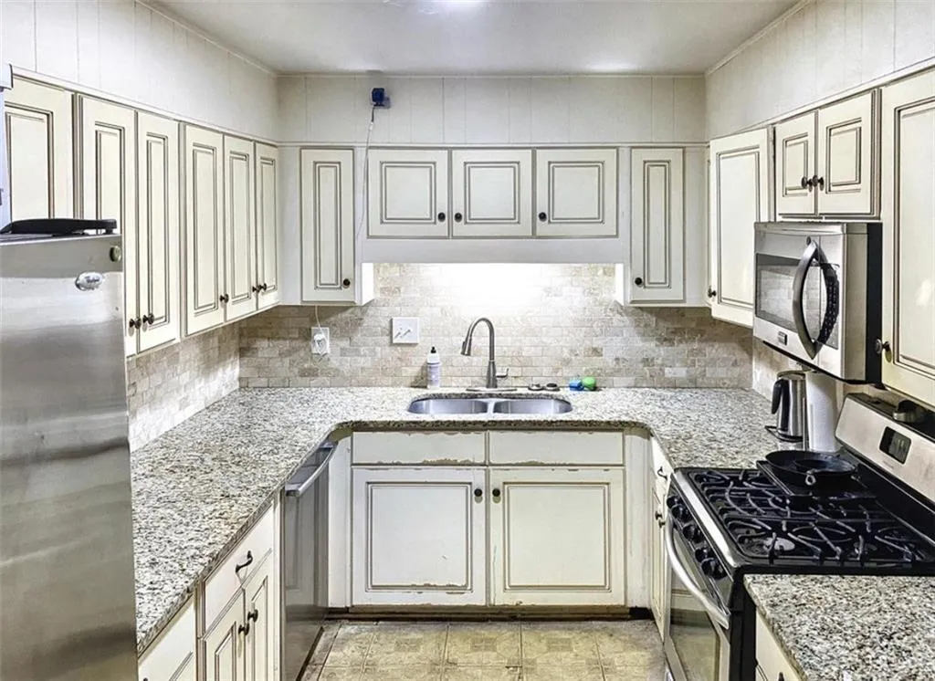 Kitchen with stainless steel appliances, light stone counters, and backsplash