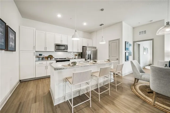 Kitchen with stainless steel appliances, white cabinetry, an island with sink, wood-type flooring, and pendant lighting
