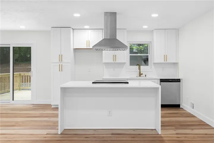 Modern kitchen featuring a central island, stainless steel appliances, white cabinetry with gold-tone hardware, wood-finish flooring, and recessed lighting