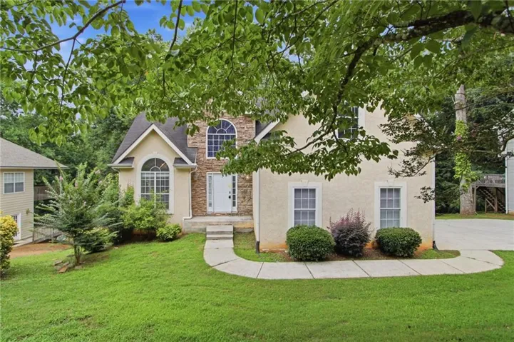 Stucco exterior featuring a prominent stone accent facade, arched windows, a white paneled front door, and a curved concrete walkway