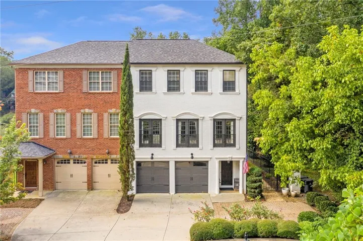 Three-story townhome featuring a brick and white facade, two-car garage, and mature landscaping