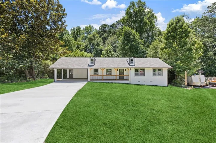 Ranch-style residence featuring a white exterior, covered front porch with wood railings, a large driveway, and a two-car carport
