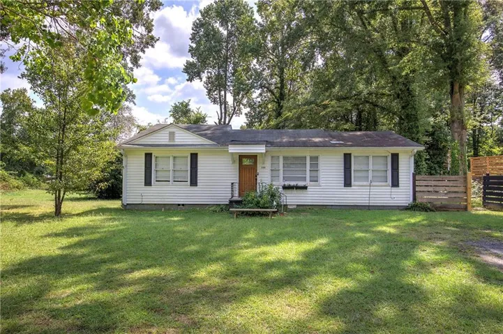 White siding exterior with a pitched roof, front entry door, multiple windows with dark shutters, and a partial wood fence