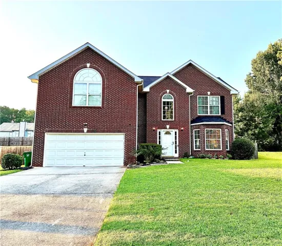 Brick Colonial two-story home featuring a prominent arched window with transom detail, two-car attached garage with white paneled door, and manicured front lawn with mature landscaping