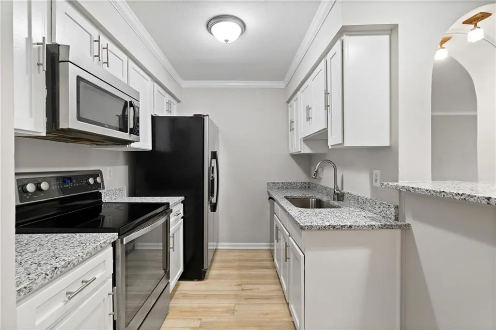 Kitchen featuring stainless steel appliances, light stone countertops, sink, and white cabinets