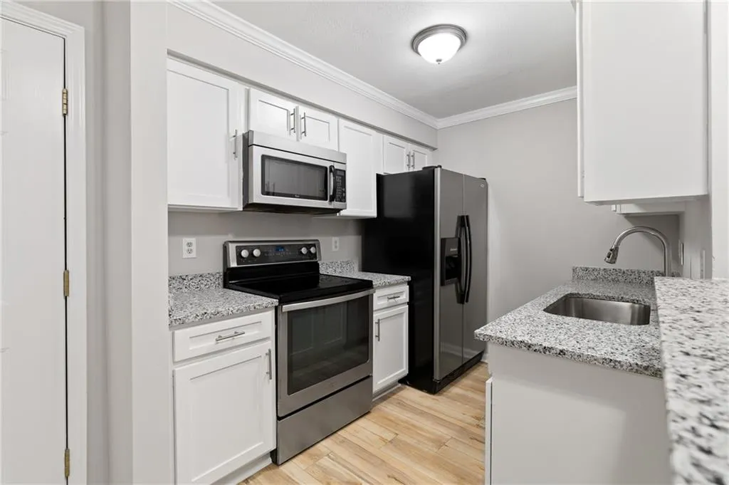 Kitchen with appliances with stainless steel finishes, sink, white cabinets, crown molding, and light stone countertops
