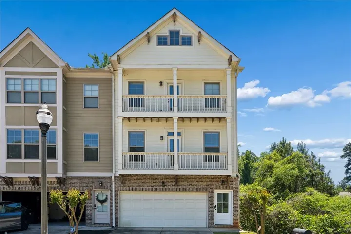 Three-story townhome featuring a two-car garage, brick facade, and two upper-level balconies with white railings