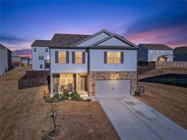 View of front of home with board and batten siding, driveway, an attached garage, stone siding, and covered porch