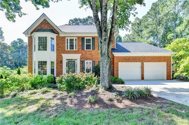 Brick exterior featuring white window trim, green shutters, and a two-car garage