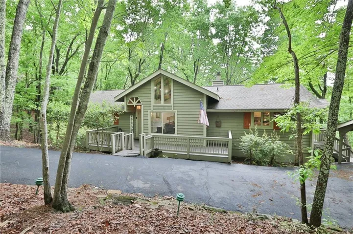 Exterior featuring light green horizontal siding, a gabled roofline, a front deck with railings, and an asphalt driveway