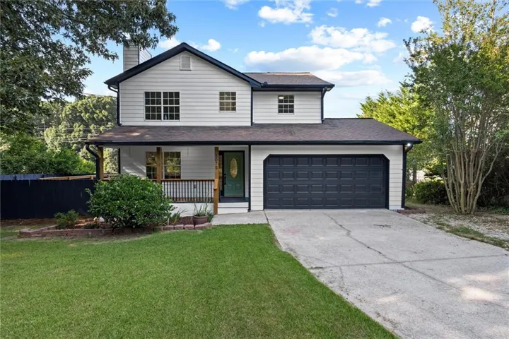 Two-story residence featuring white siding, a covered front porch with dark railings, a dark paneled garage door, and a light green front entry door