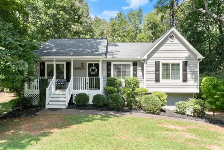 Light gray siding exterior with dark shutters, front porch with white railings, and a gabled roof