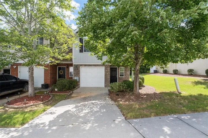 Townhome exterior featuring a white garage door, brick facade, and mature trees