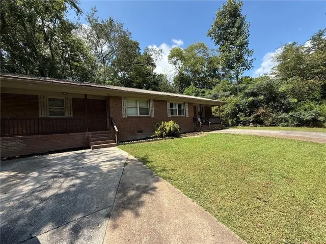 Brick exterior, covered front porch, concrete driveway, established landscaping, and mature trees