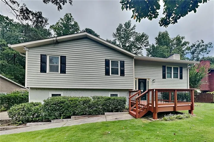 Split-level residence featuring light-colored siding, dark shutters, and a prominent front deck with a wood finish