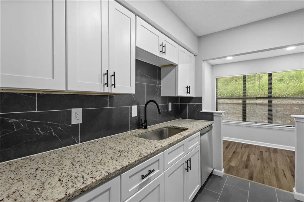 Kitchen with light stone counters, white cabinetry, backsplash, dark tile patterned flooring, and a textured ceiling