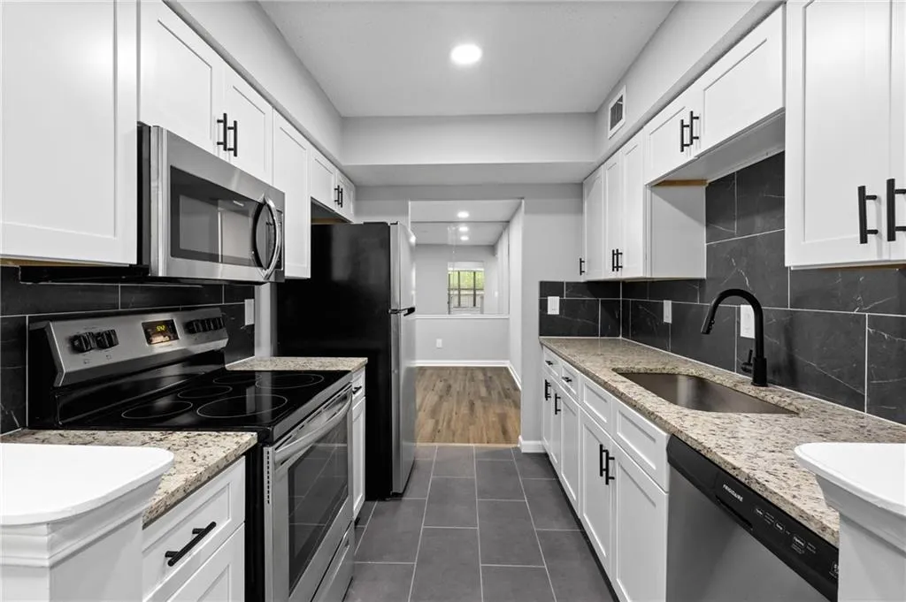 Kitchen with stainless steel appliances, light stone countertops, backsplash, dark tile patterned flooring, and white cabinets