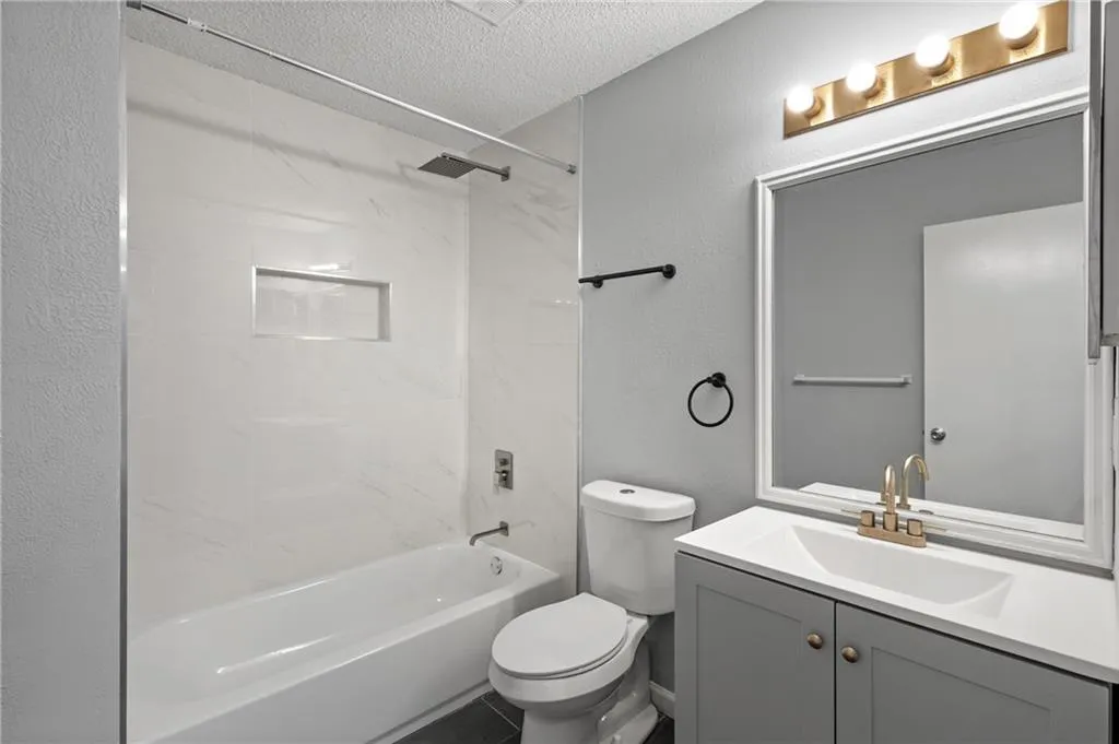 Bathroom featuring a textured ceiling, shower / washtub combination, vanity, and a textured wall