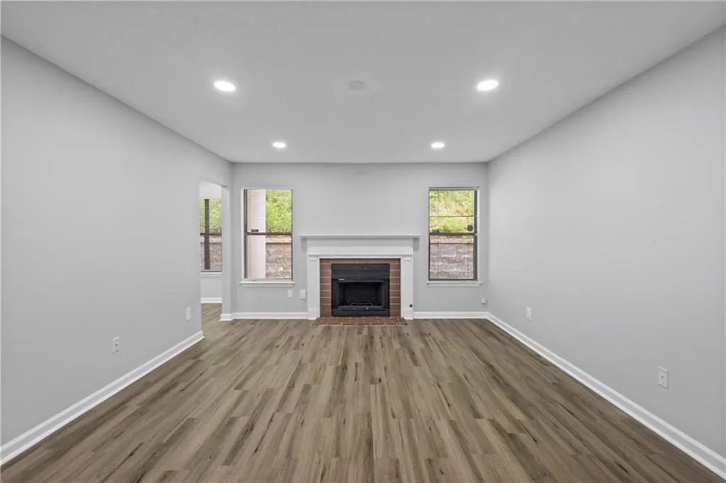 Unfurnished living room featuring dark wood-style floors, a brick fireplace, and recessed lighting