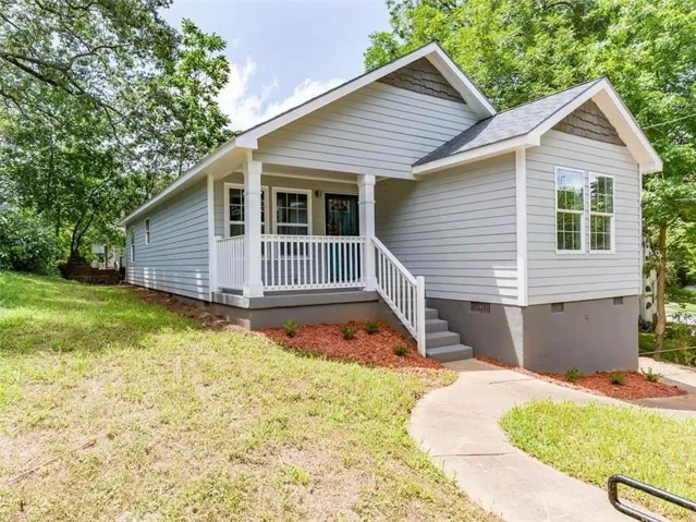 Light gray horizontal siding with white trim, covered porch with white railings, concrete walkway, and a landscaped foundation