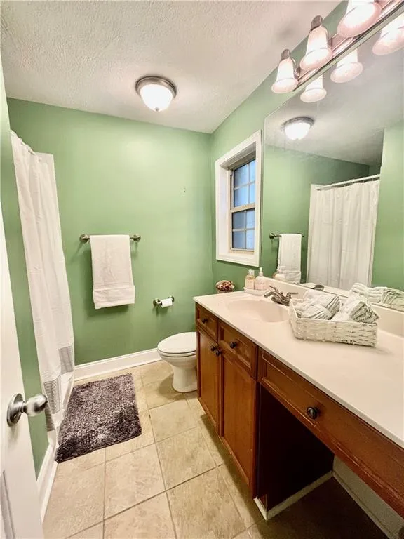 Bathroom featuring tile floors, toilet, large vanity, and a textured ceiling