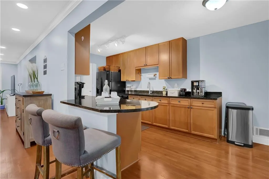 Kitchen with a kitchen breakfast bar, light wood-type flooring, black fridge with ice dispenser, dark stone countertops, and track lighting