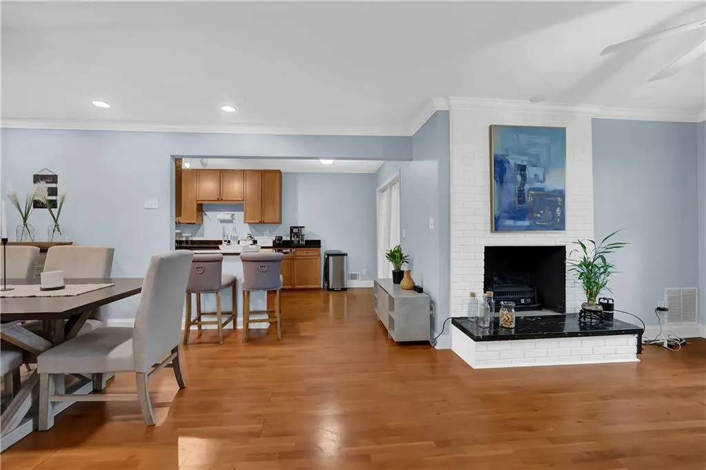 Living room featuring ceiling fan, a brick fireplace, brick wall, ornamental molding, and light hardwood / wood-style flooring