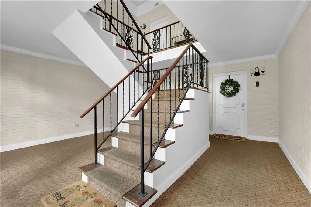 Staircase with brick wall, crown molding, and dark tile floors