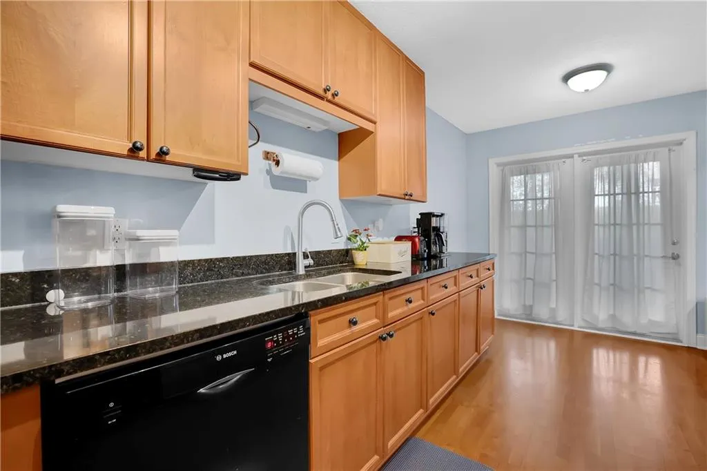 Kitchen with dark stone countertops, light hardwood / wood-style floors, dishwasher, and sink