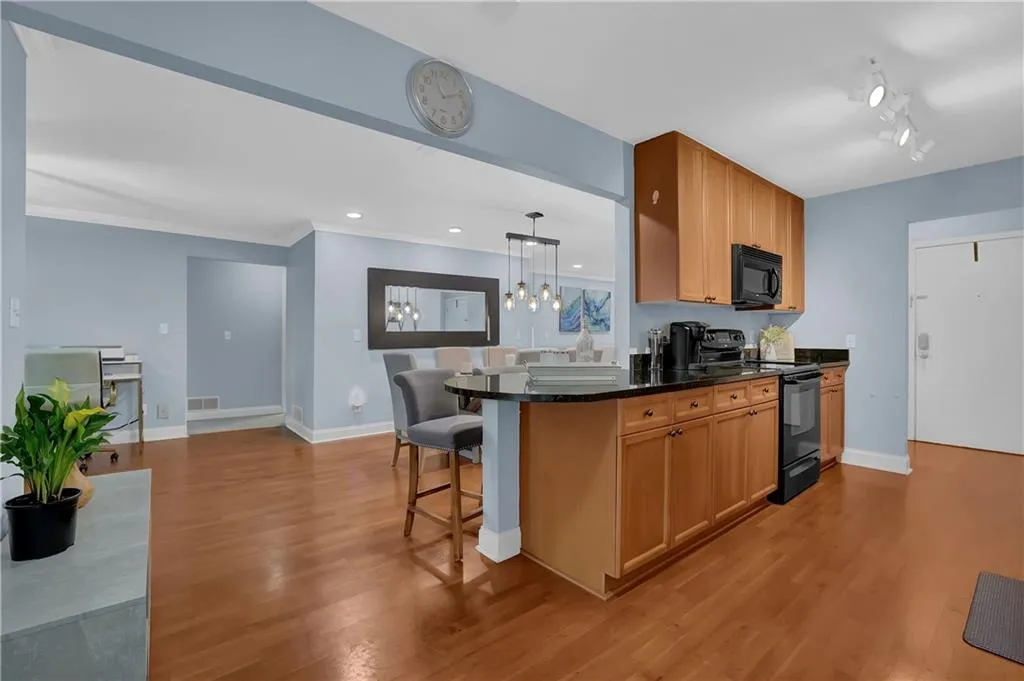 Kitchen with black appliances, rail lighting, a kitchen breakfast bar, pendant lighting, and light wood-type flooring