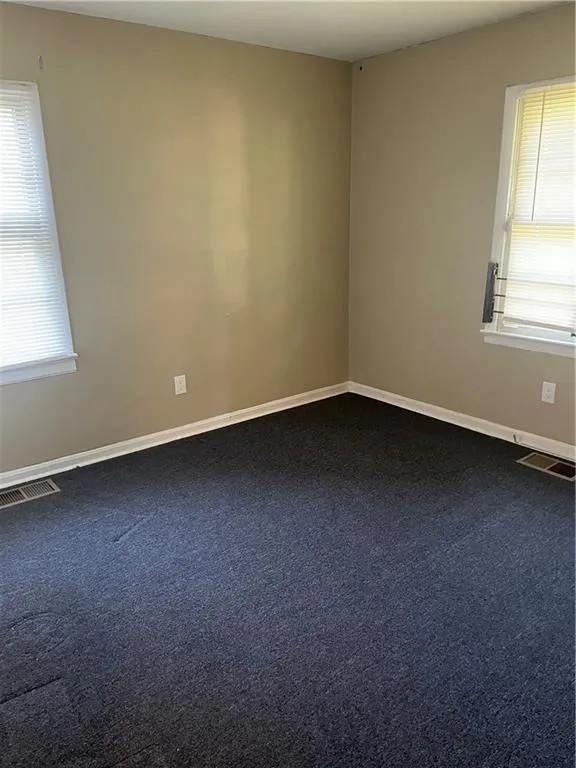 Empty room with healthy amount of natural light and dark carpet