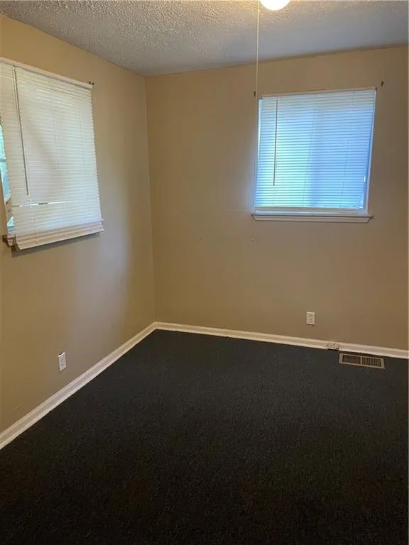 Unfurnished room with dark carpet and a textured ceiling