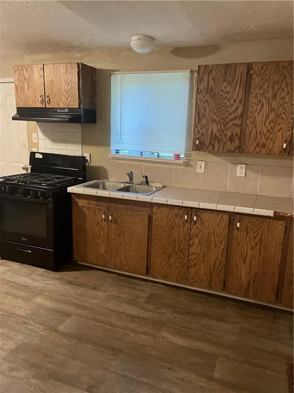 Kitchen featuring tile counters, stove, brown cabinetry, decorative backsplash, and extractor fan
