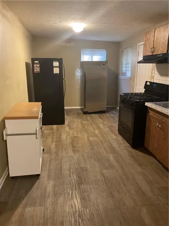 Kitchen featuring tile countertops, stove, black fridge, freestanding refrigerator, and exhaust hood