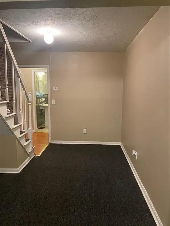 Spare room with a textured ceiling, dark carpet, and stairs
