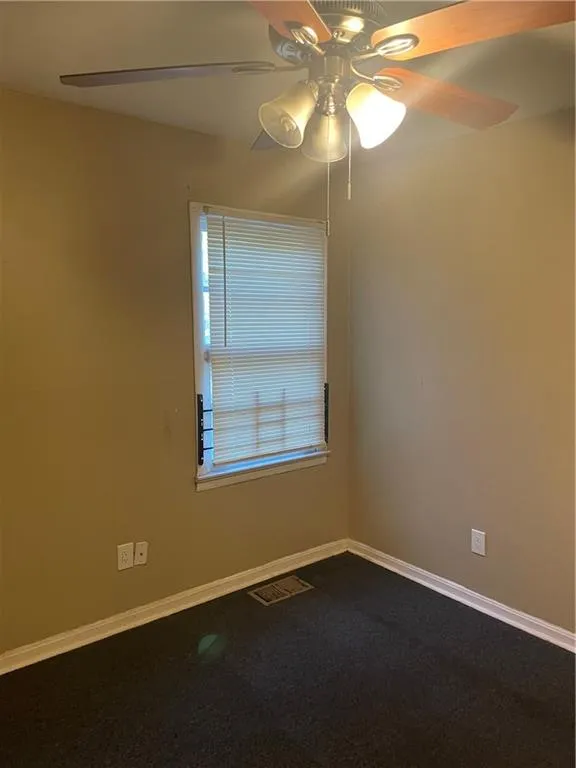 Unfurnished room featuring ceiling fan and dark colored carpet
