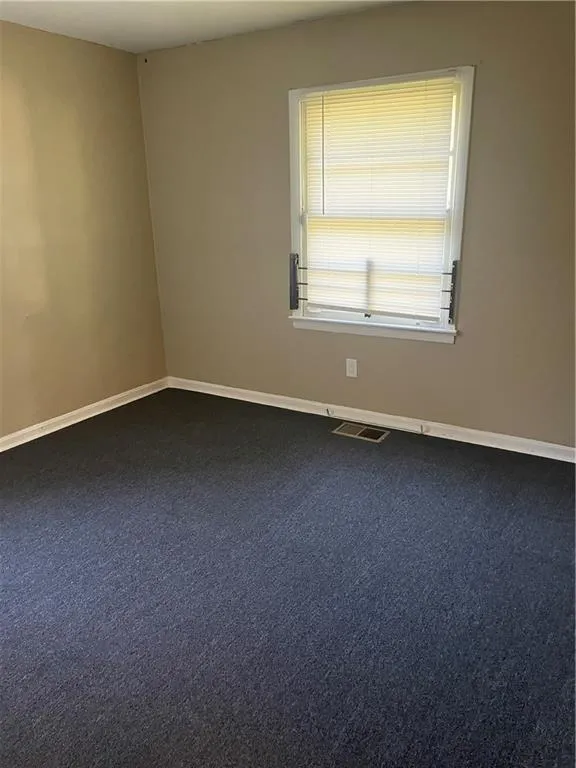 Spare room featuring baseboards and dark carpet