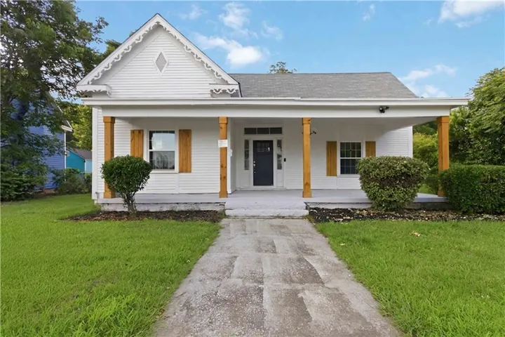 White exterior featuring a covered front porch with wood-finish columns, a dark entry door, and decorative gable trim