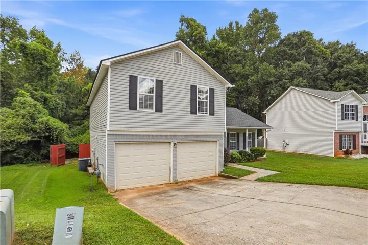 Two-story residence featuring light gray siding with a darker gray brick foundation, a two-car garage with white doors, and black louvered shutters