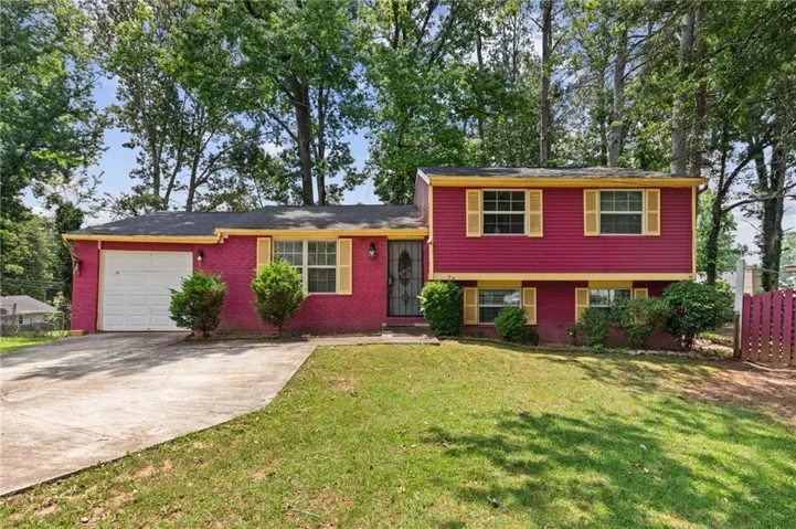 Split-level exterior featuring brick and horizontal siding, yellow window shutters, a single-car garage, and mature tree canopy