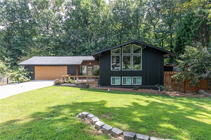 Mid-century modern exterior featuring a dark facade, a prominent front deck, multi-pane windows, an integrated two-car garage with a wood-finish door, and a manicured lawn