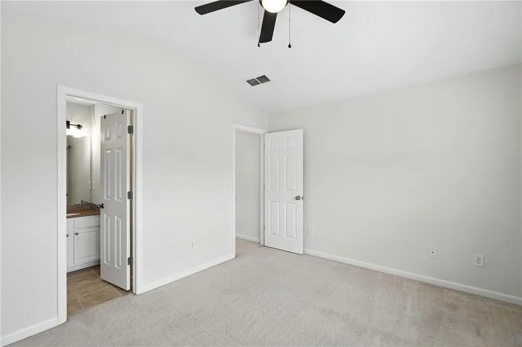 Unfurnished bedroom with light carpet, lofted ceiling, ensuite bath, and a ceiling fan