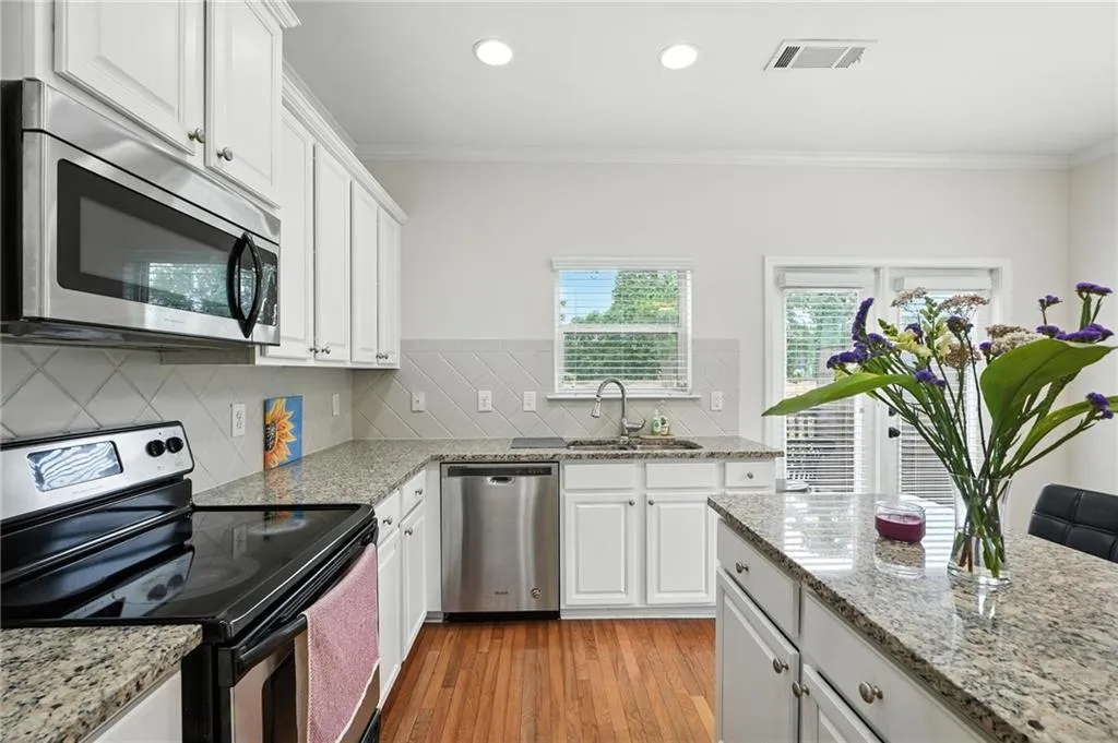 Kitchen with appliances with stainless steel finishes, backsplash, light wood-style flooring, white cabinets, and ornamental molding