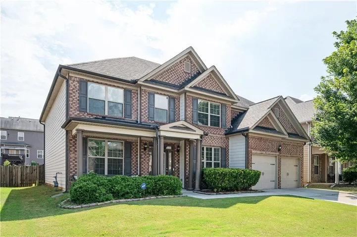 Two-story brick facade with decorative gables, covered front porch with columns, and an attached two-car garage