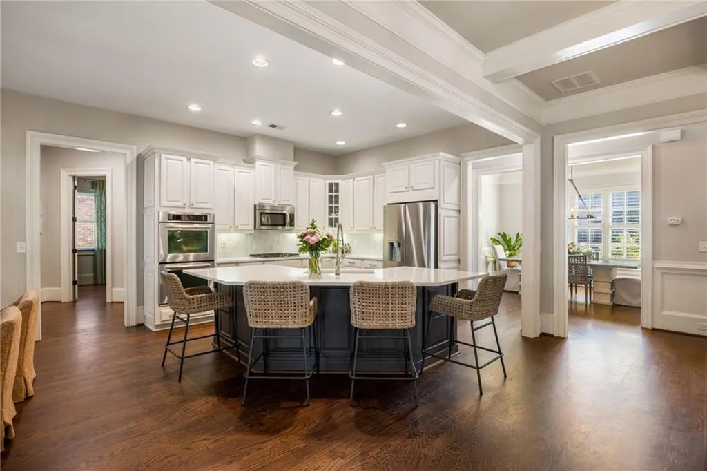 Spacious kitchen featuring an oversized island with countertop seating, white perimeter cabinetry, stainless steel appliances, and wood-finish flooring