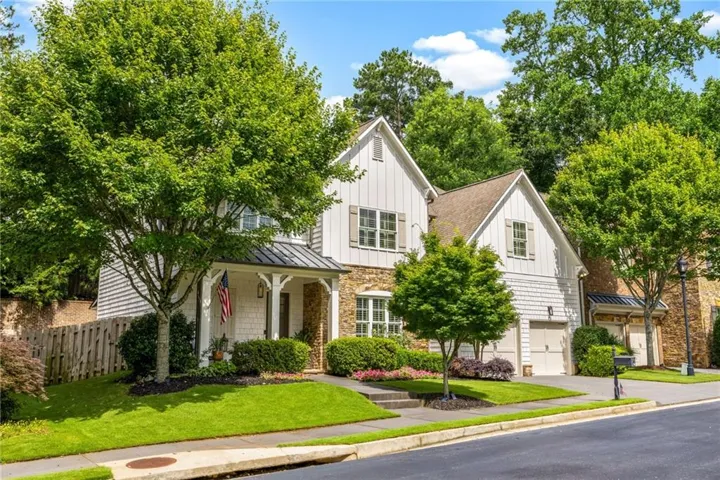 Two-story residence featuring a covered front porch, an attached two-car garage, stone accents, and a gabled roofline